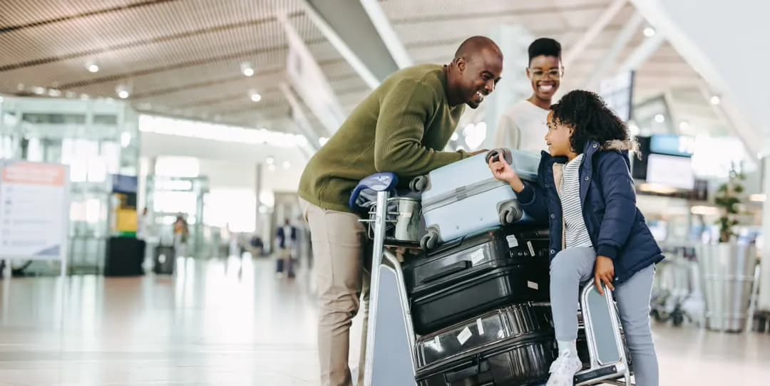A family laughing together beside a luggage trolley in an airport terminal